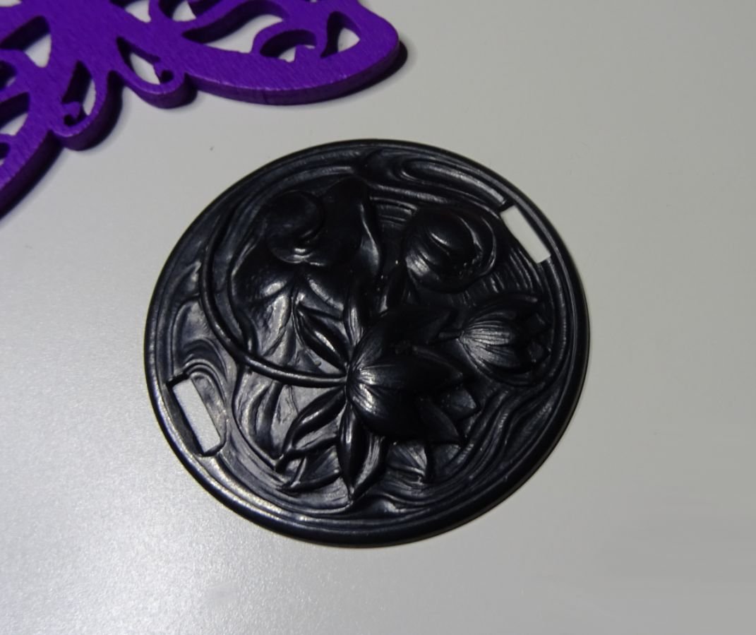 Medaljong i svart metall i relief med sidoband 